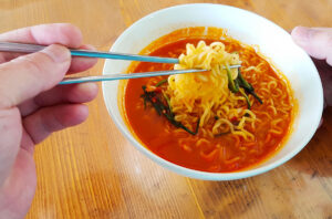 My left hand picking up ramen noodles from a bowl with chopsticks.