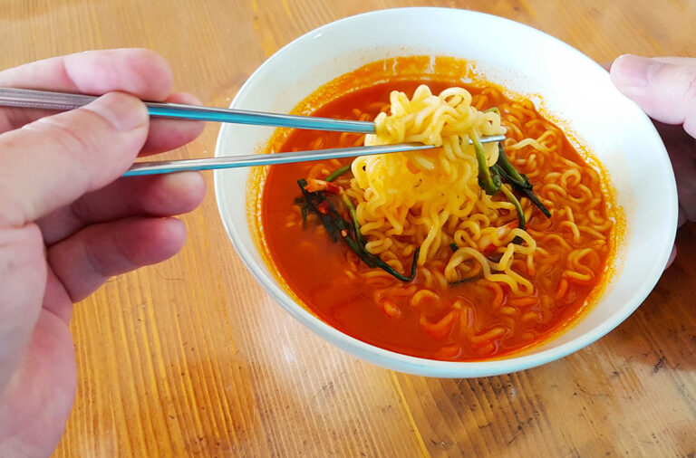 My left hand picking up ramen noodles from a bowl with chopsticks.