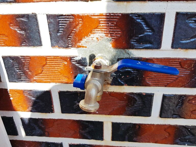 The blue outdoor faucet (spigot) that needs to be winterized, attached to an exterior wall.