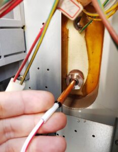 Sliding the new sensor probe into its dedicated dry-well tube inside the boiler.