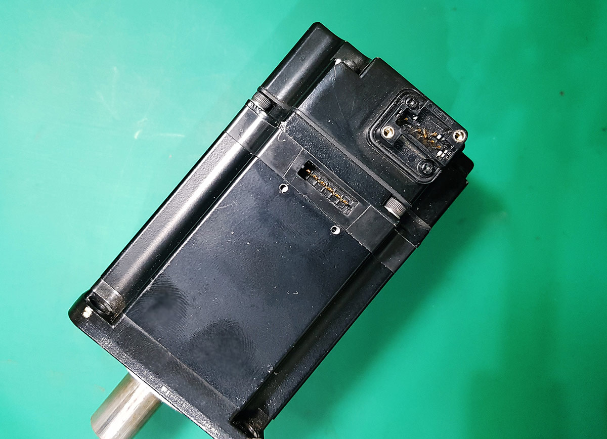 The returned Yaskawa servo motor lying on a work surface, with its encoder connector port visible.